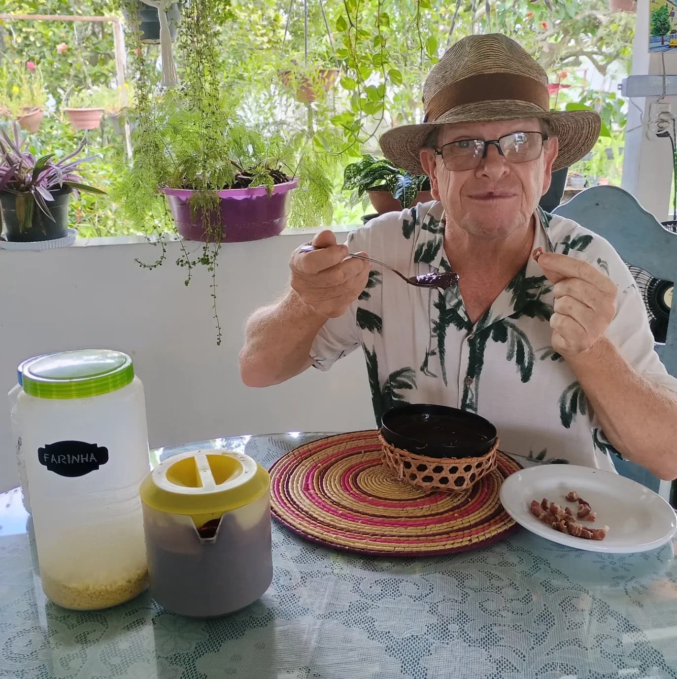 Marc na varanda de casa, com uma cuia de açaí, o pote de farinha e as plantas atrás.